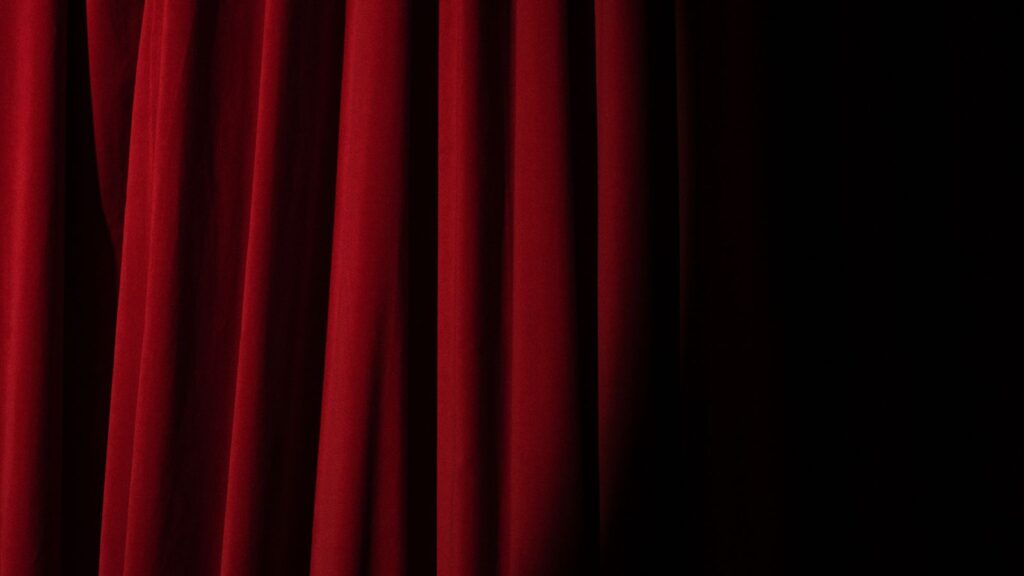 Dramatic theater stage with rich red velvet curtains under a spotlight