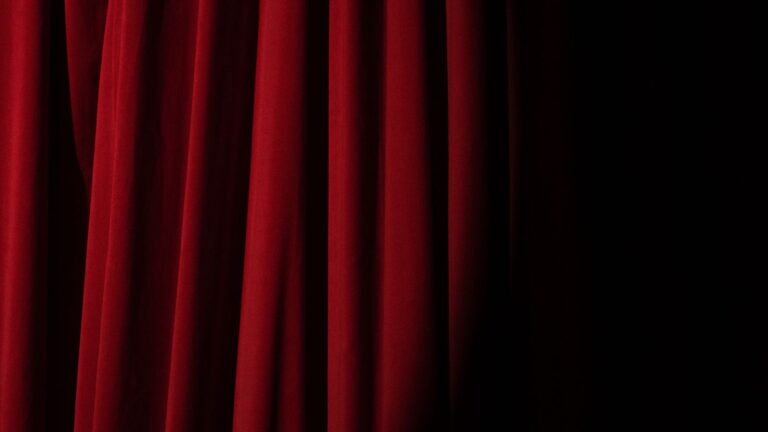Dramatic theater stage with rich red velvet curtains under a spotlight