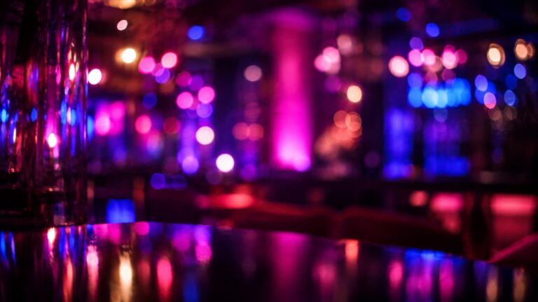 Abstract neon-lit lounge with glowing pink, purple and blue bokeh reflections evoking queer nightlife