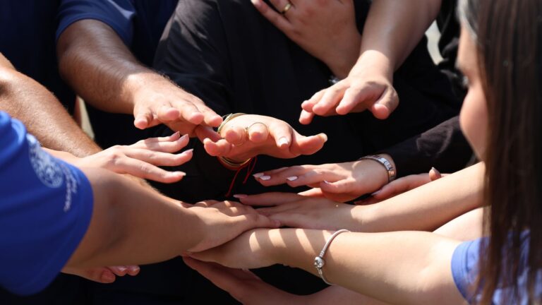 Several hands joined together in warm sunlight, symbolizing connection and trust